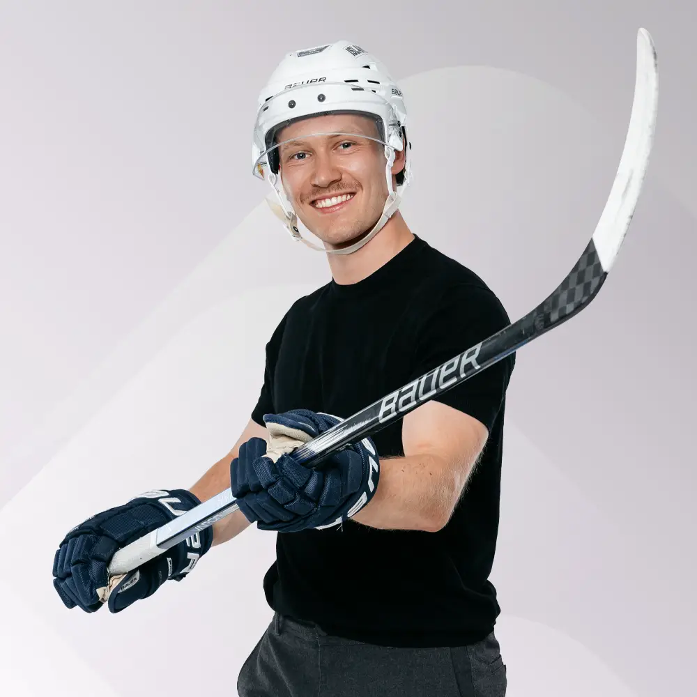 Mann in Eishockey-Ausrüstung mit Helm und Schläger lächelt in die Kamera